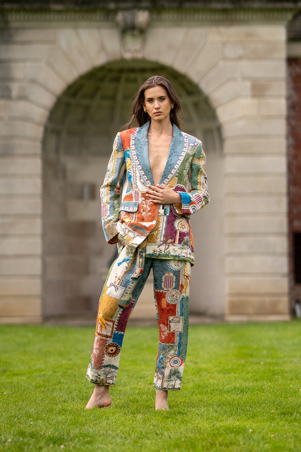 Person wearing a colorful patchwork outfit standing in front of a stone building.