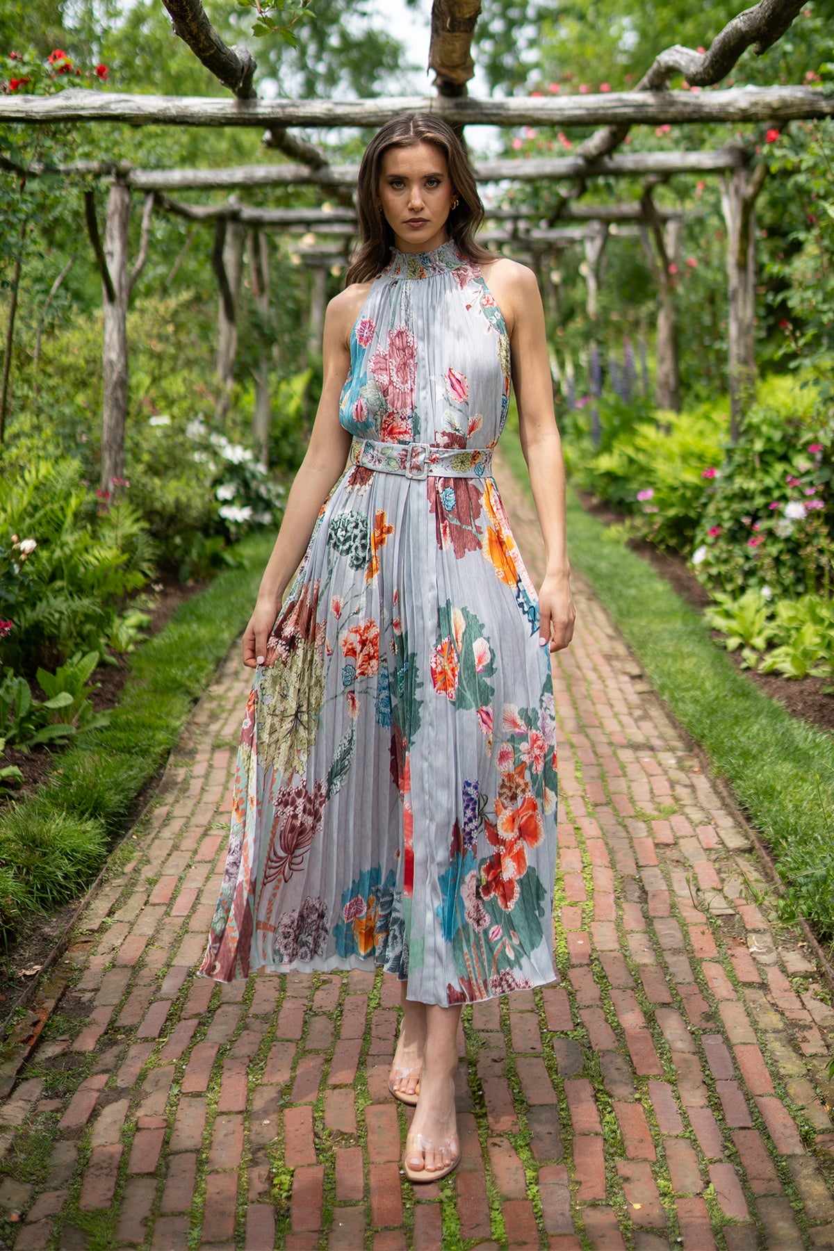 Woman in a floral dress standing on a brick path in a garden