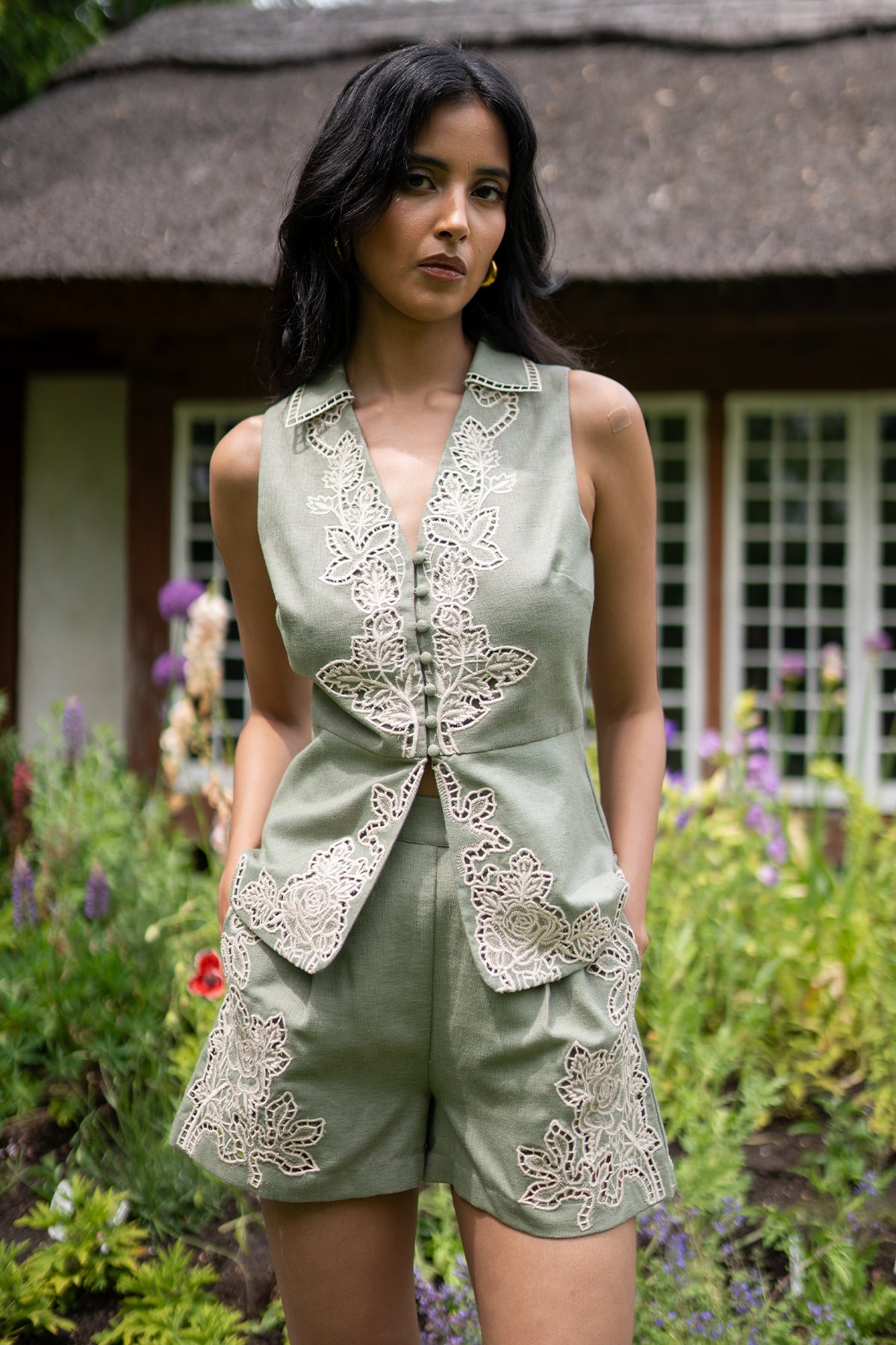 Woman wearing a green embroidered outfit standing in a garden.