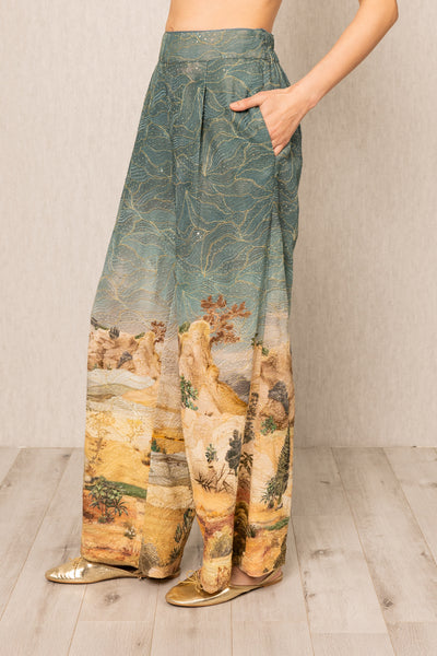 Person wearing a pair of wide-leg pants with landscape print on a neutral background
