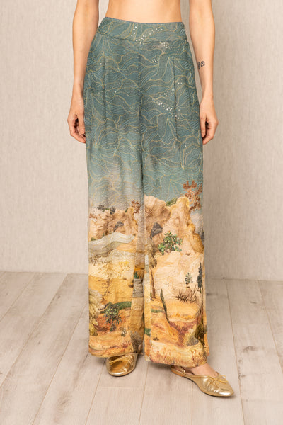 Person wearing a pair of wide-leg pants with a landscape print on a plain background