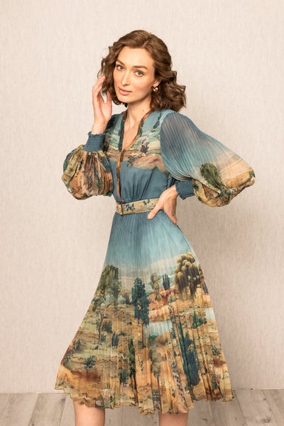 Woman wearing a scenic dress with long sleeves and a belt, standing against a plain background.