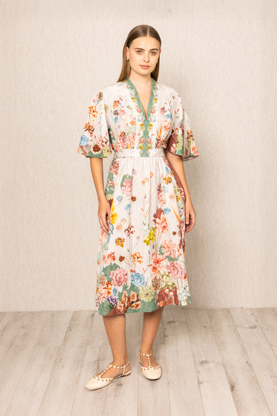 Woman wearing a floral V- neck dress standing against a plain background