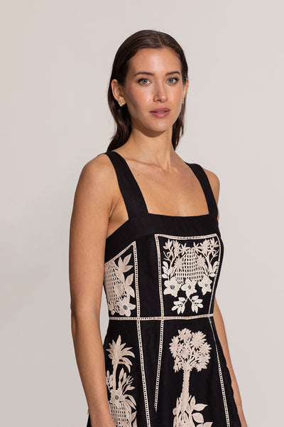 Woman wearing a black dress with white floral embroidery on a plain background