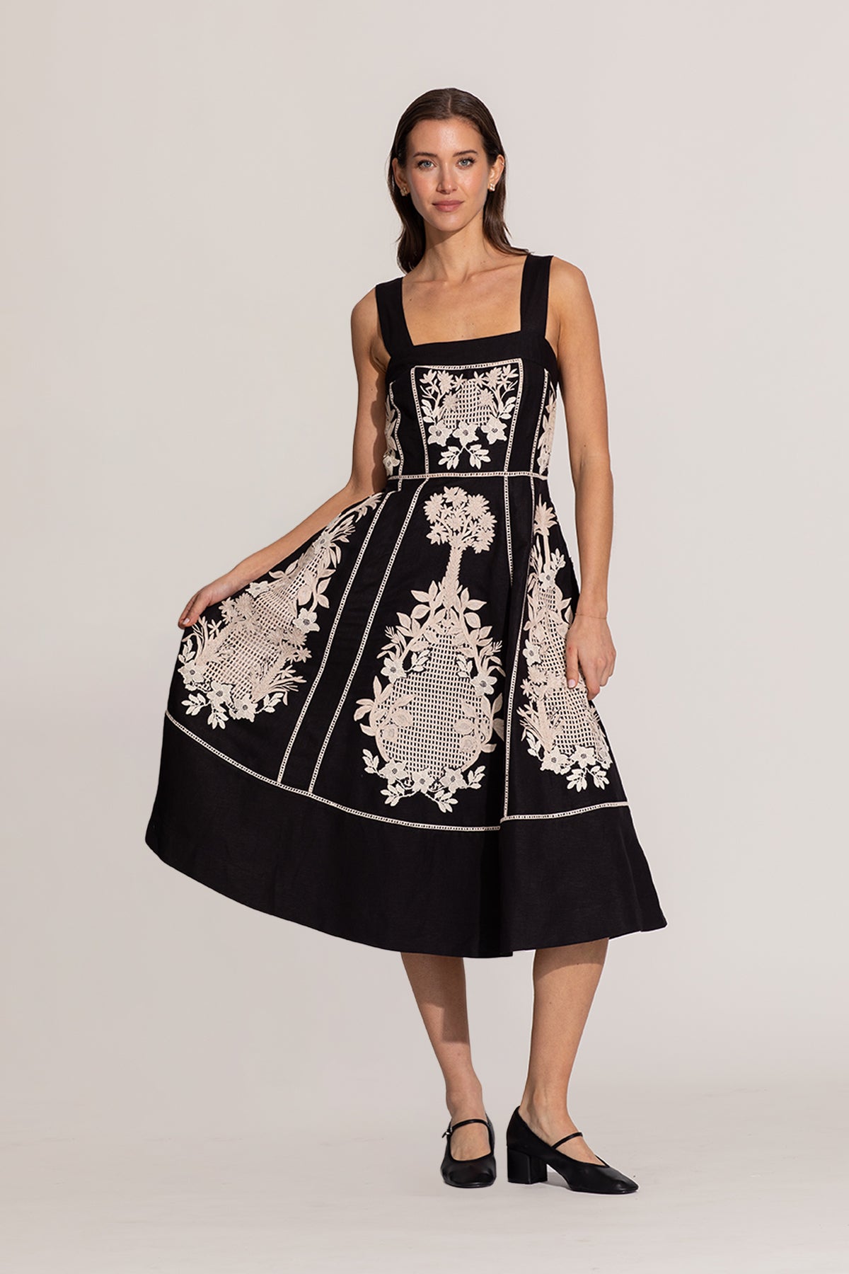 Woman wearing a black dress with white floral embroidery on a plain background