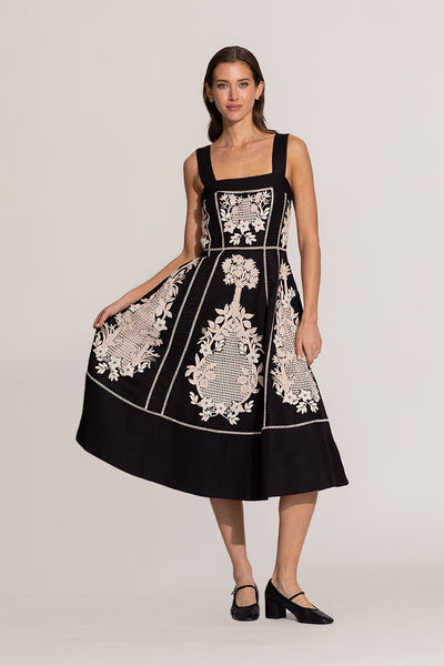 Woman wearing a black dress with white floral embroidery on a plain background