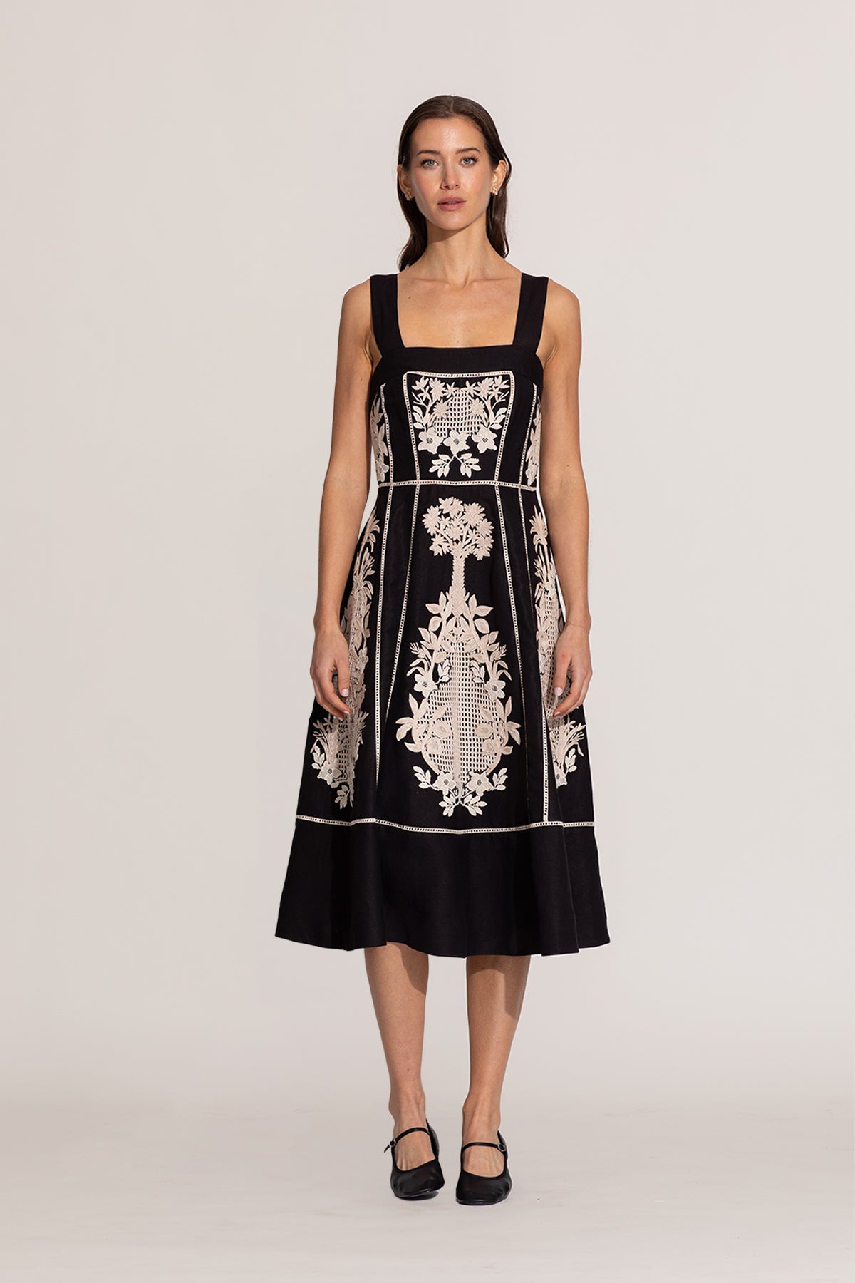 Woman wearing a black dress with white floral embroidery on a plain background